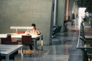 Man studying alone at a modern desk in a quiet, well-lit office or library space with concrete walls and sleek furniture.